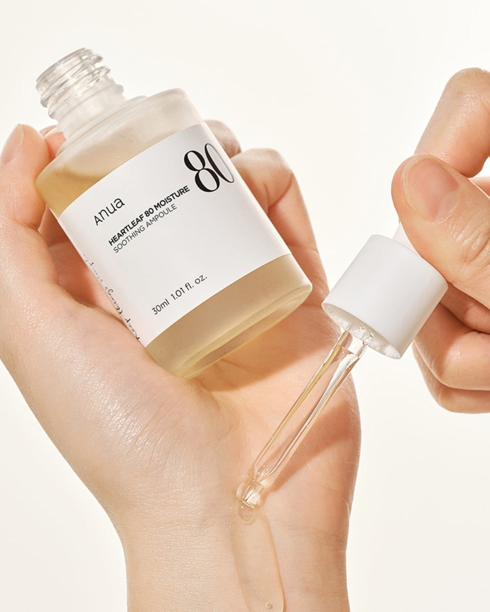 Anua Heartleaf Soothing Ampoule, with a clear liquid visible inside the glass container, placed on a white plate with a leaf on the top and the brand name 'Anua' mentioned.

