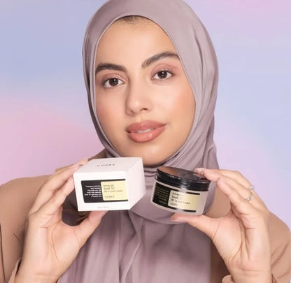 Woman holding a jar and box of skincare product against a pastel background

