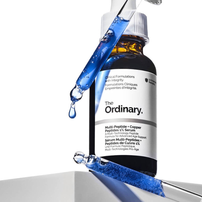 The Ordinary serum bottle with blue liquid being dispensed onto a white background

