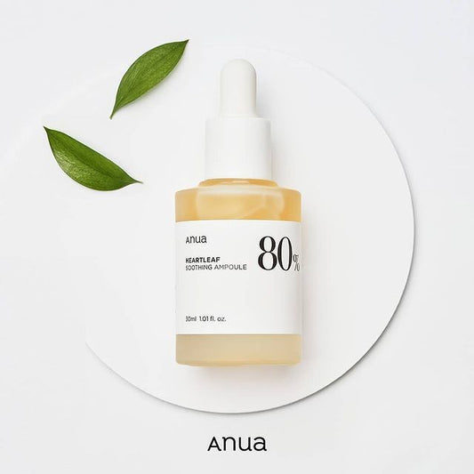 Anua Heartleaf Soothing Ampoule, with a clear liquid visible inside the glass container, placed on a white plate with a leaf on the top and the brand name 'Anua' mentioned.

